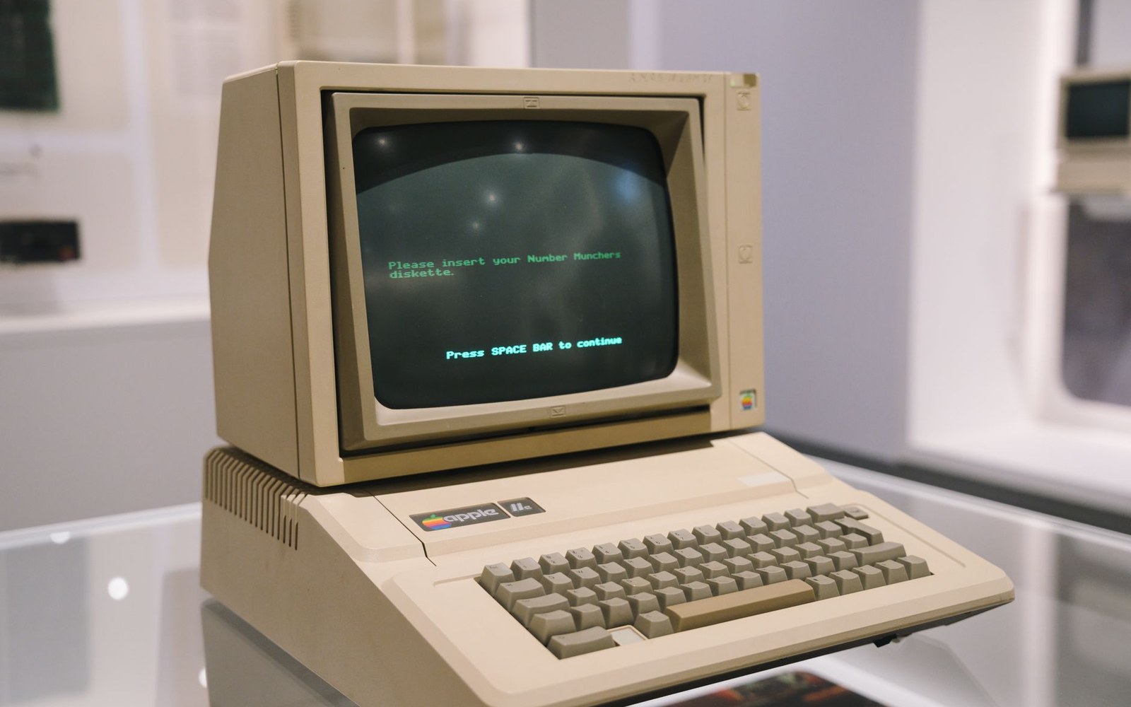 A 1980s school computer laboratory with a row of Apple II computers on standard-issue tables, monitors on, room unoccupied