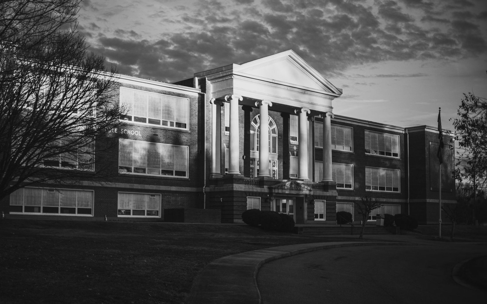 Brick school building with tall white columns and a triangular pediment at dusk