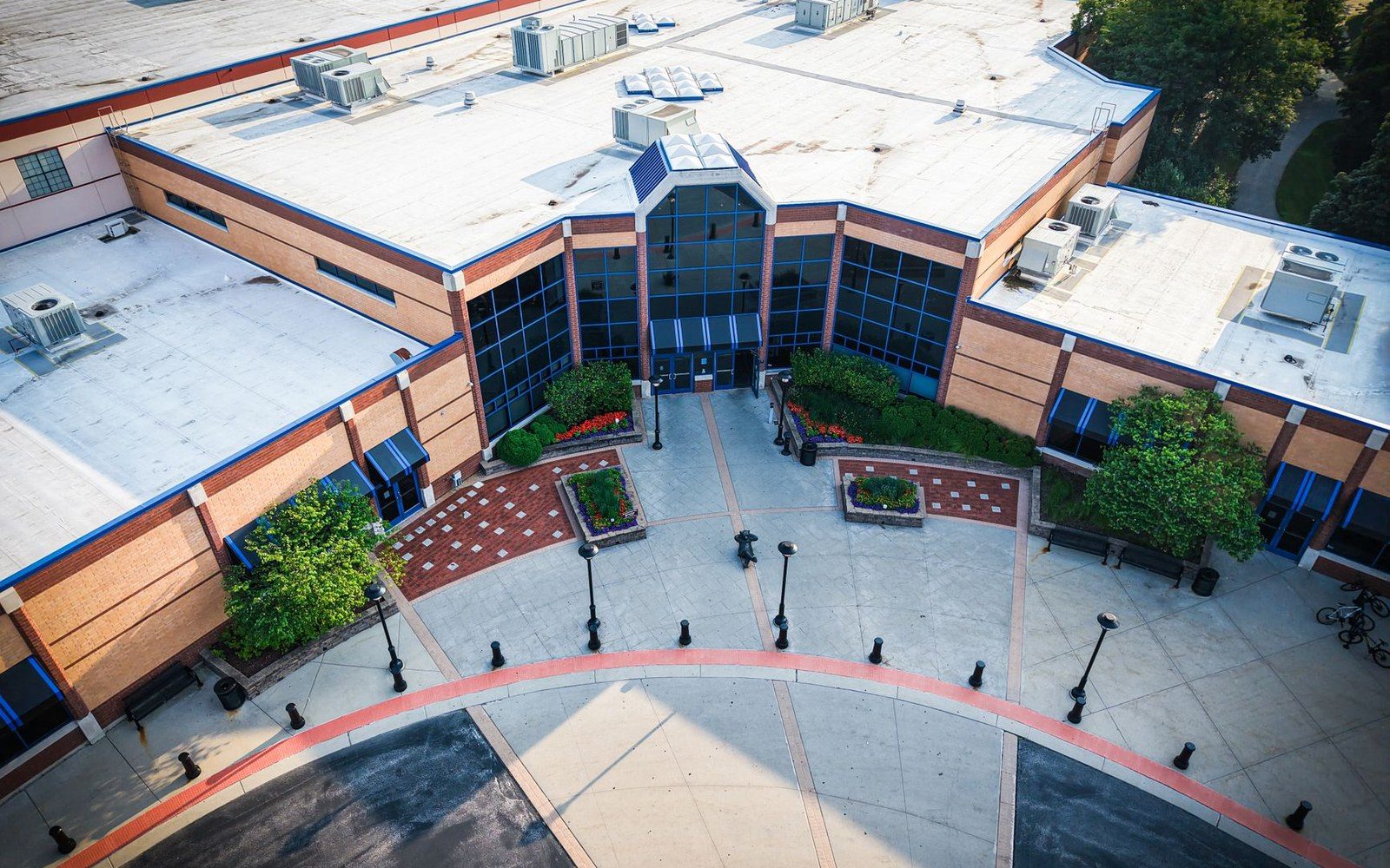 Aerial view of a brick building's entrance with rooftop HVAC units and a paved plaza