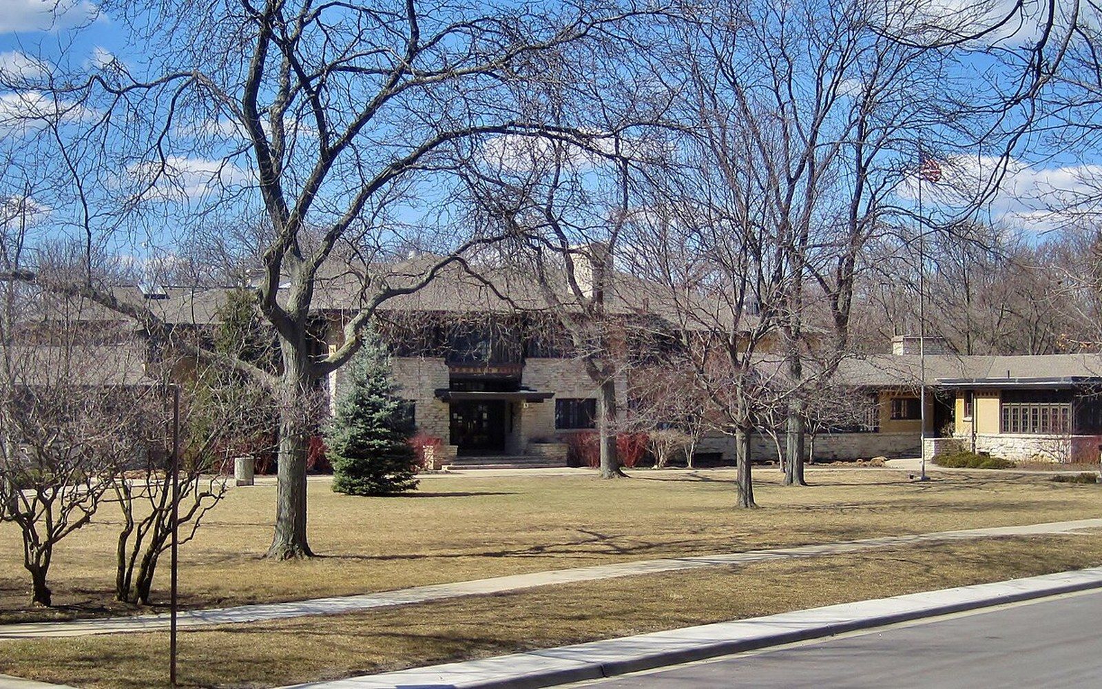Low brick school building with a flagpole, surrounded by bare trees on a lawn