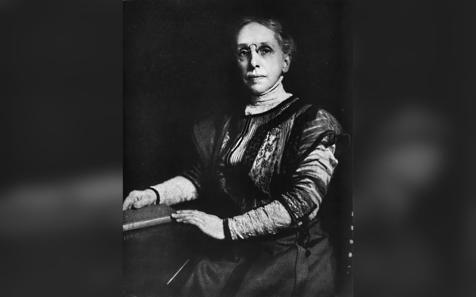 Black-and-white portrait of a woman in Victorian-era dress seated at a table
