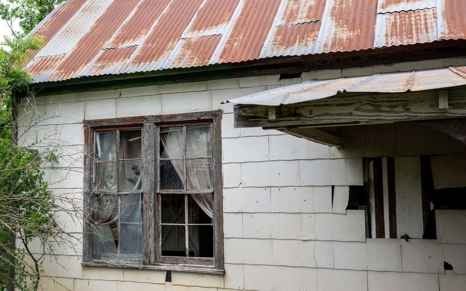Rusted tin roof and torn siding on an abandoned building with a broken window
