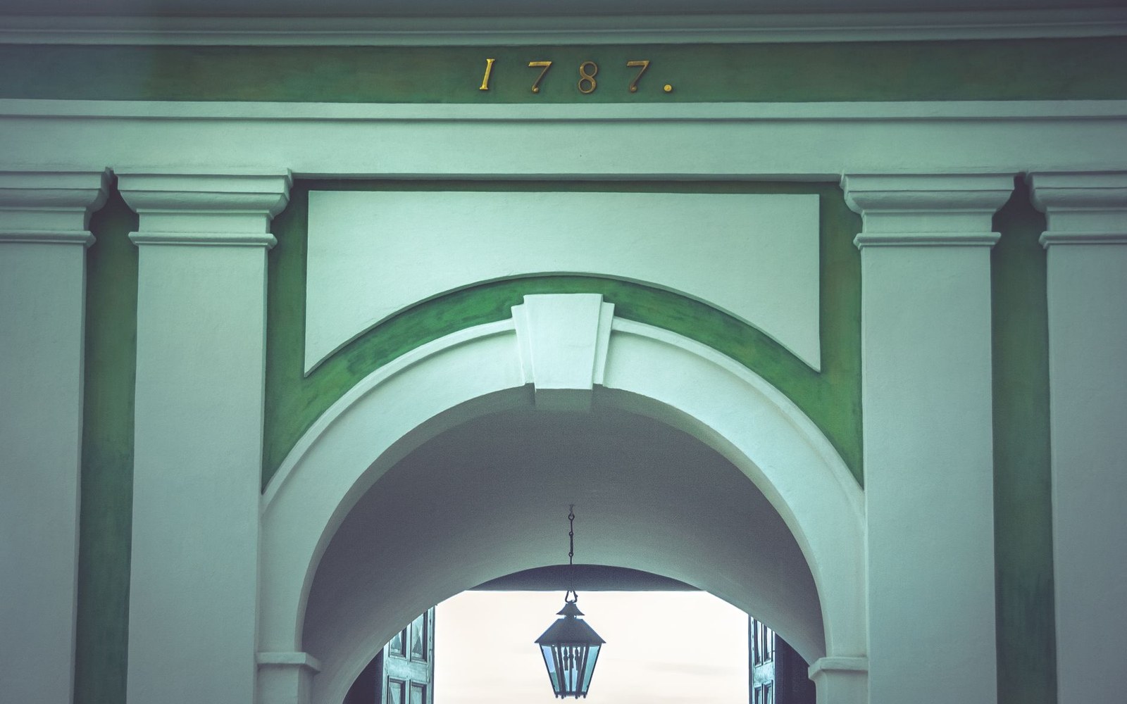 Archway with gilded date 1787 above green trim, hanging lantern visible beneath the arch