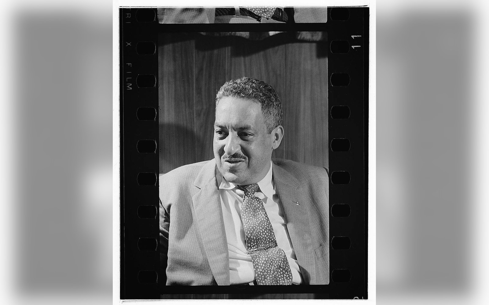 Black-and-white film negative frame showing a smiling man in a suit and polka-dot tie
