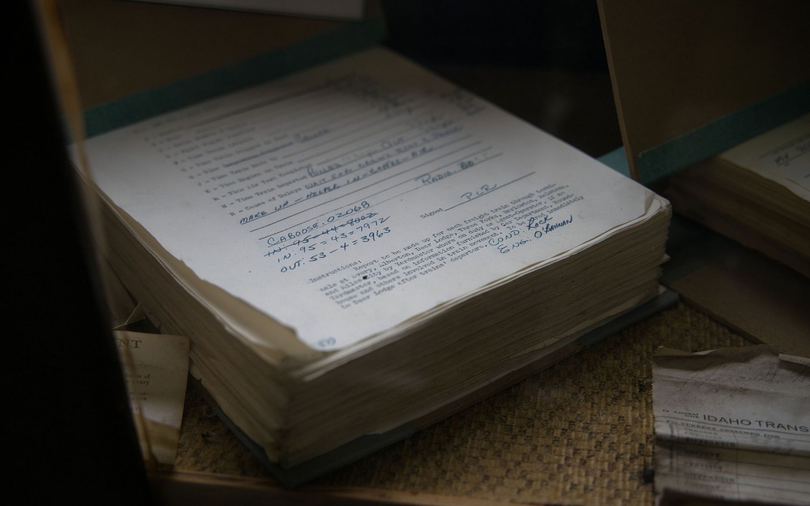 An open ledger with handwritten entries sits atop a stack of aged paper records