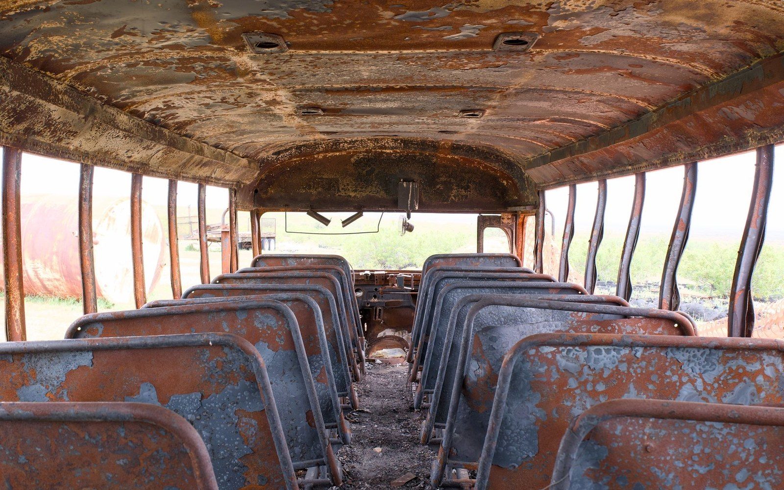 Rusted interior of an abandoned school bus with rows of decaying seats